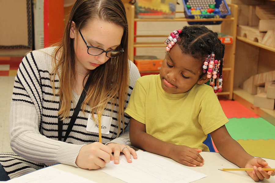 Freshman Lizzy Morales draws with a child at the Upper Room during Freshman Day of Service.