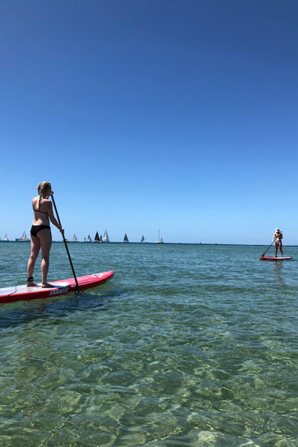 Senior Anna Tomka paddle boards alongside Alisha Centrone at Rye beach in Victoria.