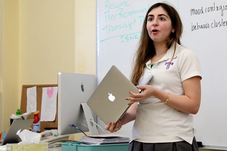 Senior Loulya Alabed holds her laptop at the front of a classroom as she reads questions and leads a discussion between maisons April 12.