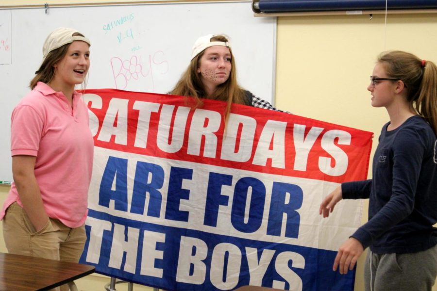 Sophomores Mia Legato, Maggie McKinney, and Paxton Misemer hold up a “Saturdays are for the Boys” flag during their Beggining Debate class Sept. 17. The spirit week theme was Sion School for Boys.