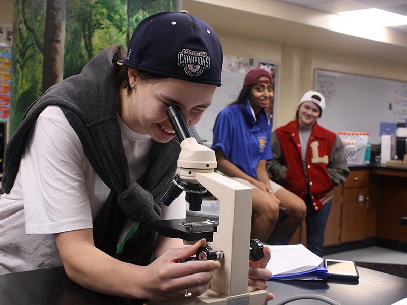 Senior Megan Broomfield looks at an amoeba through a microscope during her AP Biology class Sept. 17 as seniors Elizabeth Puthumana and Victoria Farrington look on dressed to the theme of the day. The theme was Sion School for Boys.