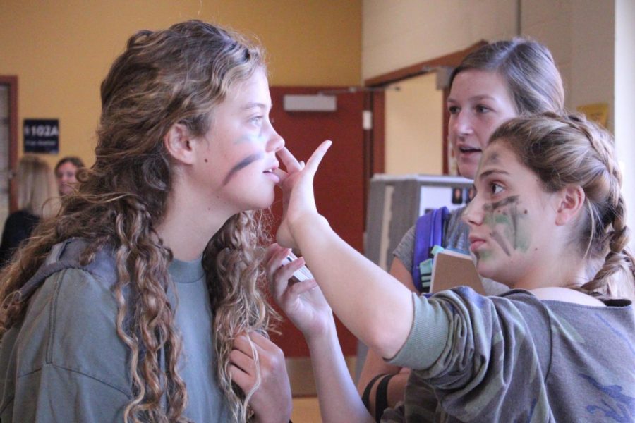 For the second day of spirit week, sophomore Lorelei Mathews paints camoflauge face paint on sophomore Ruby Wright before school Sept. 18.