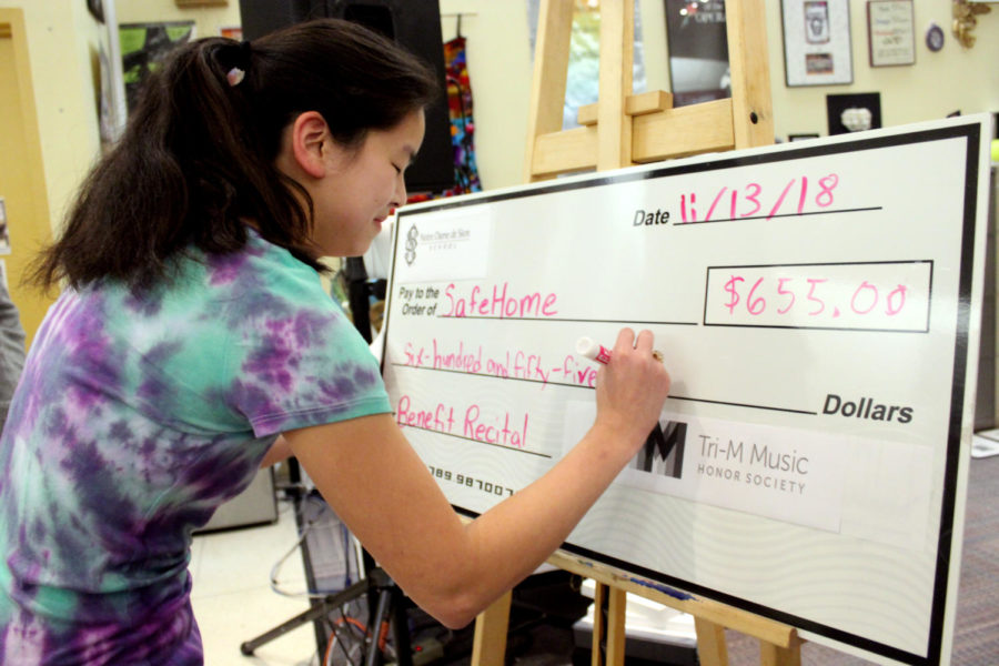 Tri-M president senior Sarah White signs a check of $655 for Safe Home after the benefit concert Nov. 13.