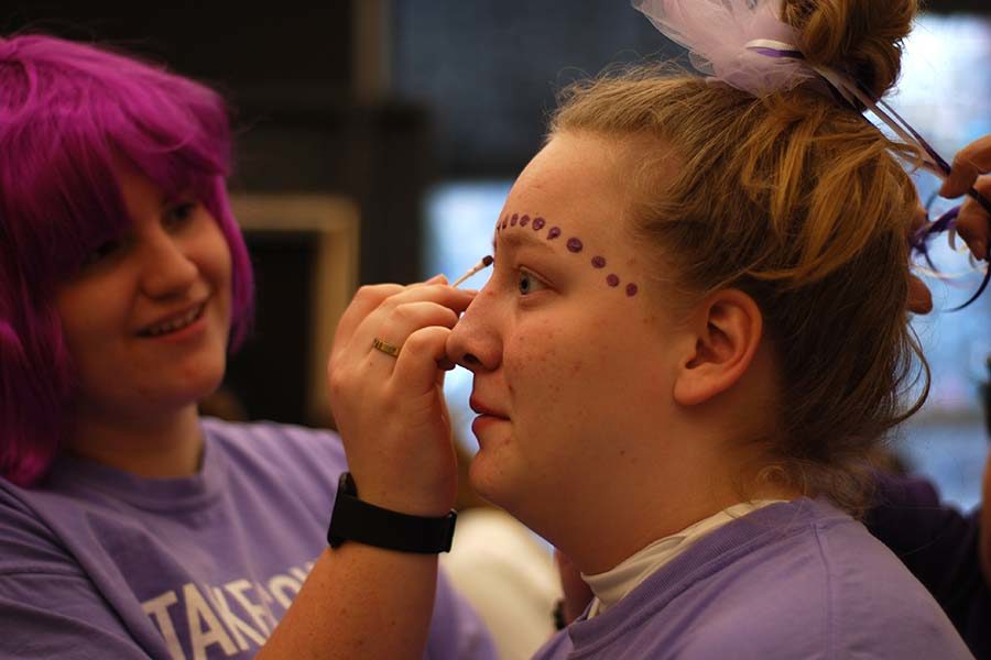 Before the St. Teresa’s Academy basketball game Feb. 21, senior Scream Team leader Emma Cruciani paints purple face paint on fellow senior Scream Team leader Savannah Friedebach. The theme for the game was purple and white to increase accesibility for students, according to President Alicia Kotarba.