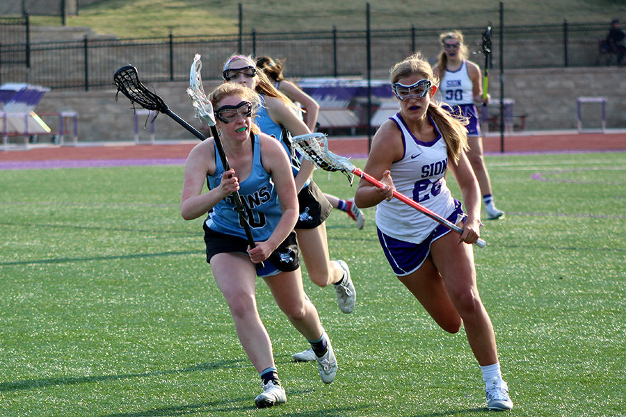 After saving the ball, sophomore Mikayla Gunther runs toward the goal while playing against Blue Valley High School at home March 27. The game ended in a loss for the team with a final score of 15-6. 