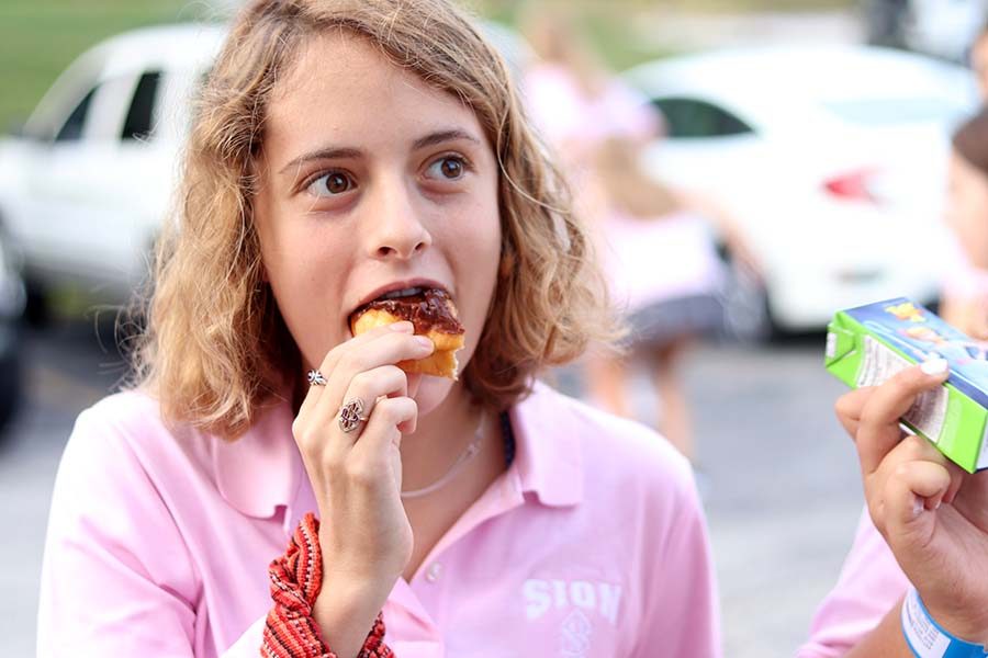 Senior Phoebe Mullen eats a chocolate glazed donut at the annual senior tailgate. For the tailgate, senior students volunteered to bring various breakfast snacks including bagels, chocolate milk, fruit, orange juice, donuts, coffee and more. 