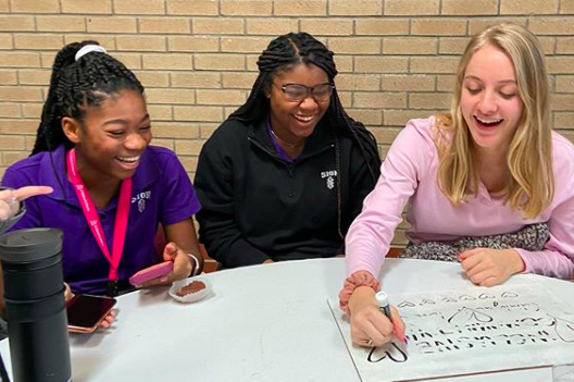 As the kick off to Catholic Schools Week, seniors and freshmen met up for a Peer Ministry meeting during lunch and study hall Jan. 27. Freshman Makaila Traylor, senior Maya Scott and senior Elizabeth Crabtree write on the white board their answers to the discussion question "Why I love Sion."