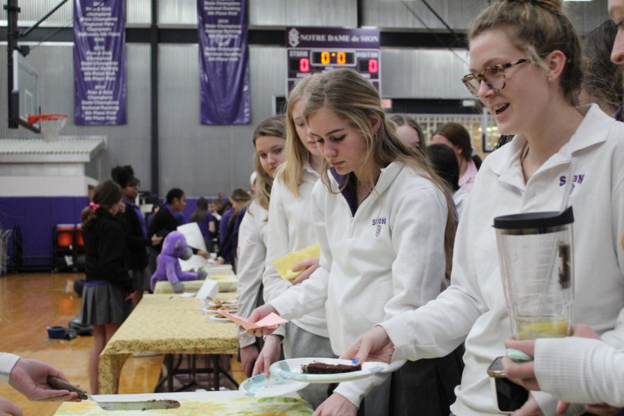 Junior Zoe Zorn and freshman Veda Renzulli are served cake samples from senior Sela Kincaid at the bake-off Feb. 21.