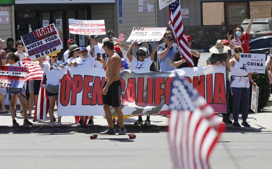 A skateboarder films protesters along Mission Blvd. in Pacific Beach during A Day of Liberty rally on Sunday, April 26, 2020. The protesters were against the government shutdown due to the coronavirus.