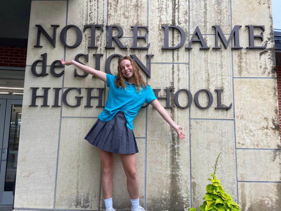 Senior Betty Christianson celebrates her first week at a new school in front of the main entrance. Christianson, who transferred from St. Teresa's Academy, made the decision to transfer in the summer.