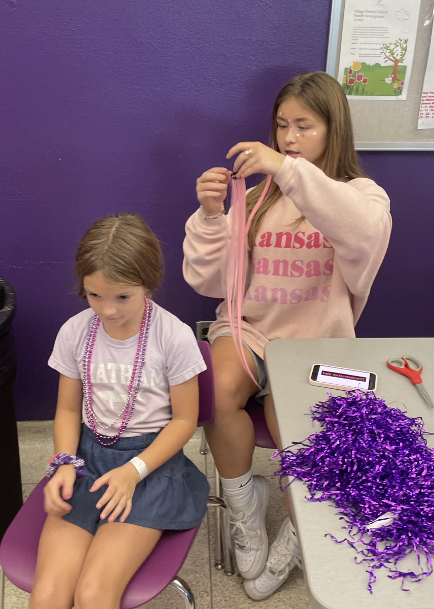 Senior Elise Daugherty applies pink hair extensions onto a guest from the Tailgate for the "Barbie" theme of the Volleyball Tailgate on October 5.