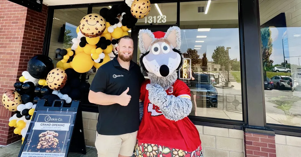 Posing with KC wolf, Prior Chiefs football player Jordan Devey takes a photo in front of his new franchise business Cookie Co. The grand opening consisted of free cookies, special gifts, and a twisted soda happy hour with a charitable purpose. 
Photo By: Kadey Cramer for The Telegraph