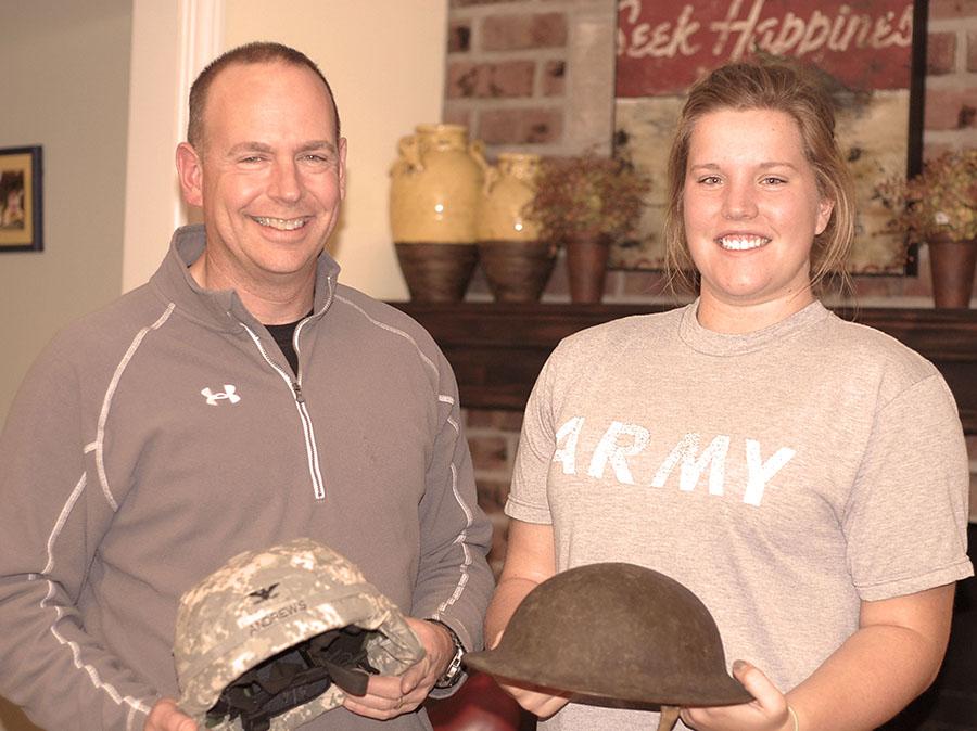 Senior Katie Andrews holds her great-grandfather’s WWI helmet while her dad, Colonel Phil Andrews, holds his helmet from his recent deployment in Iraq.