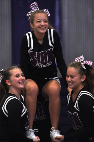 Junior Taylor Spies and senior Anna Lillis hold up freshman Savannah Childress during the cheer team's pep assembly performance Sept. 4. 