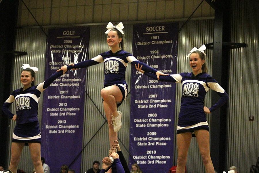 Sophomores Caroline Bono and Maddi Clark help hold up Freshman Liz Oltjen during a halftime performance.