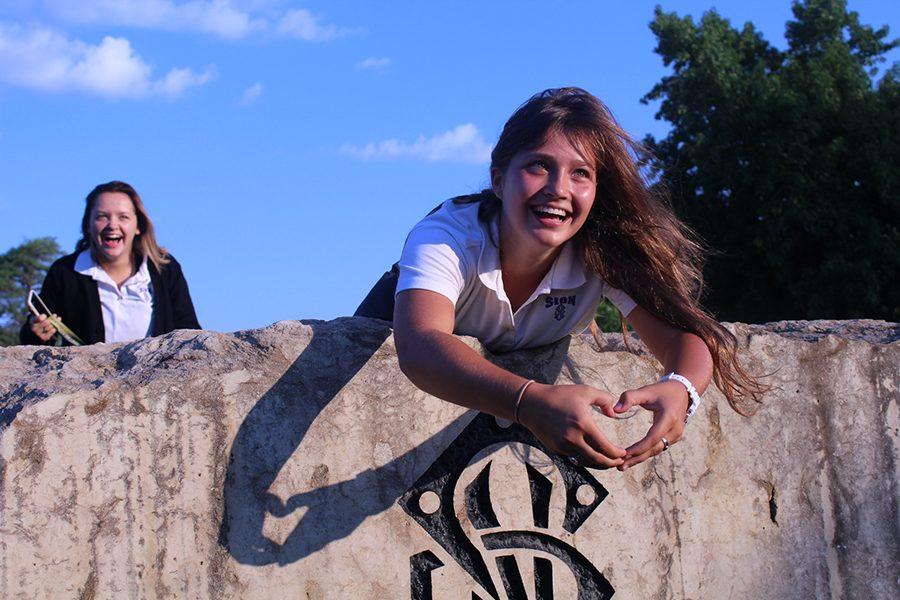 Senior Zoe Trouve  shows her school pride by making a heart shape over the school insignia.