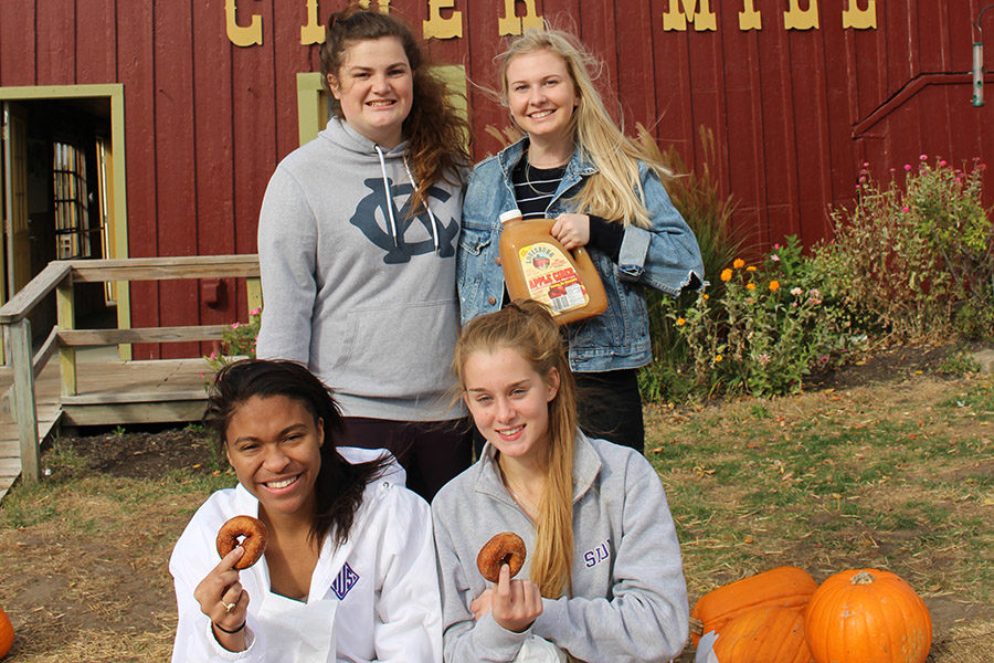 Junior Kaitlin Jones and seniors Kelly Nugent, Phylicia Barner-Lewis and Anna Tomka pose for a picture holding donuts and cider. 