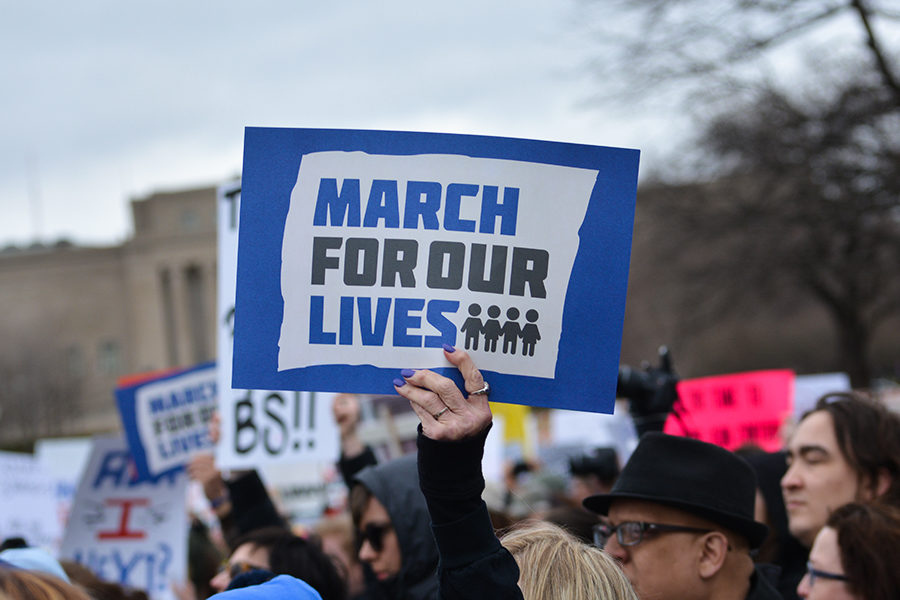 Asked by the speaker for the crowd to hold their signs in the air, a woman puts a sign given to her at the march in the air at the March For Our Lives held at Theis Park in Kansas City, Missouri March 24.