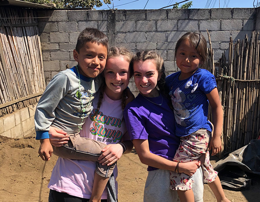 Alumna Molly Conway '19 and senior Meg Wilkerson hold Guatemalan children while working on building a concrete stove for the family in San Andres Itzapa March 11, 2019. This year's trip to Guatemala has been postponed due to concerns surrounding the coronavirus. 