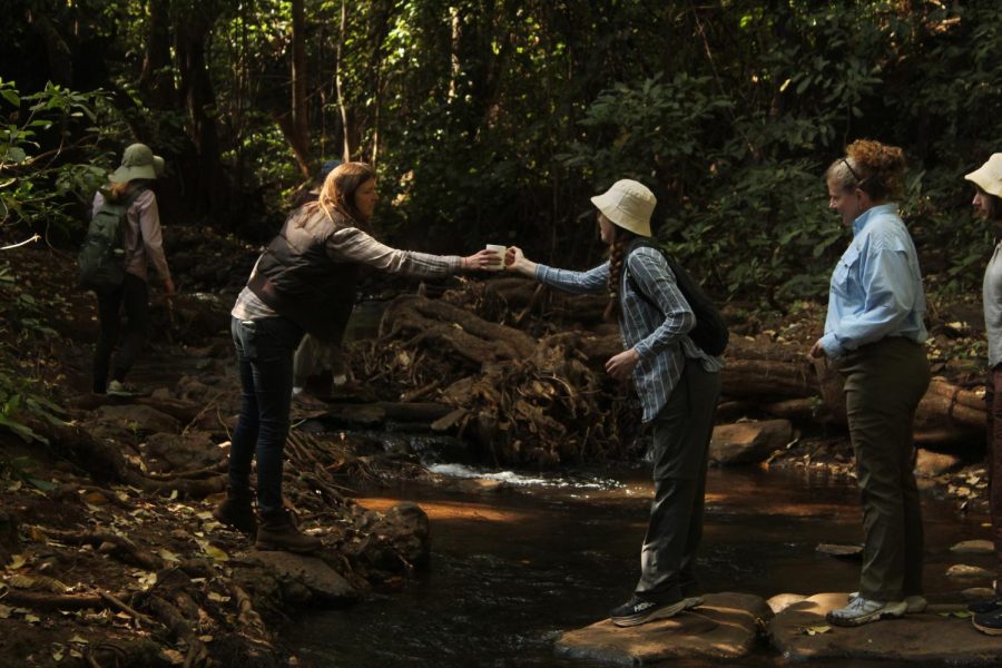 Junior Ginger Griffiths hands her coffee mug to Kate Spencer in order to jump across the creek.