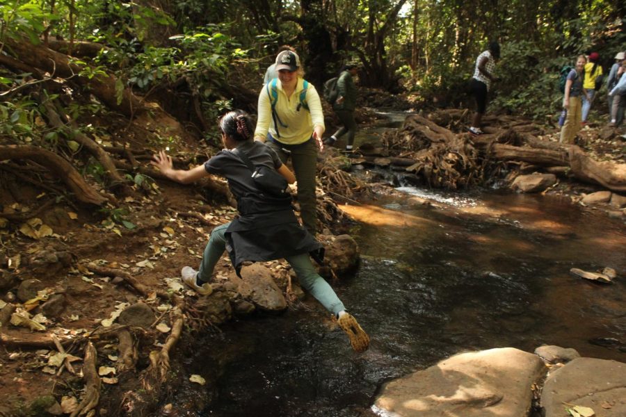 On a hike Junior Lucy Wittek waits for Emilie Lai to jump across a creek.